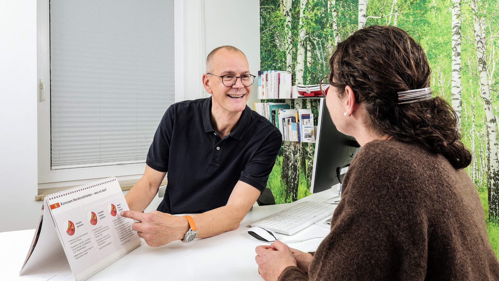 Arzt erklärt weiblicher Patientin an seinem Schreibtisch sitzend etwas